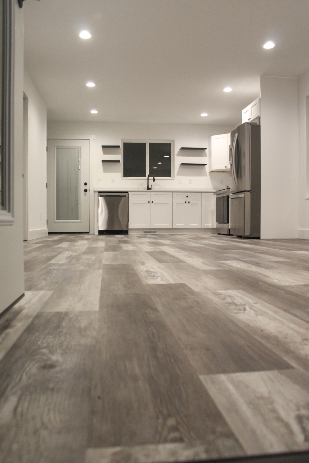 Finished white kitchen with floating shelves and wood-look flooring